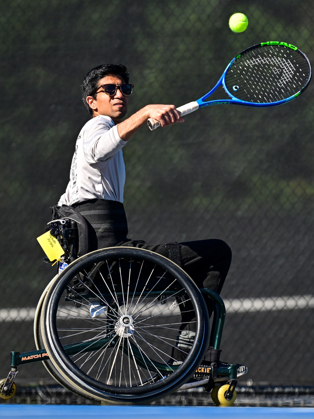 Prasidh Arora striking a forehand in his tennis chair, the ball in the air above the racquet.